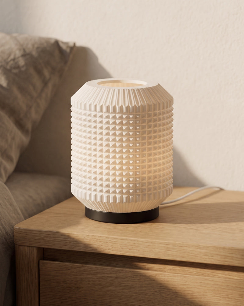 Greta table lamp lit on an oak nightstand, studded bone-white body glowing warm